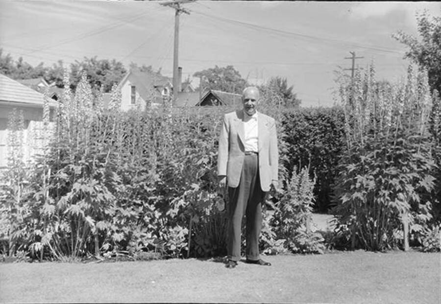 Photograph depicts an older Frank B. Robinson in formal clothes standing outside in front of bushes.