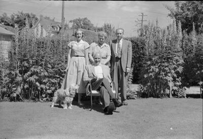 Family photograph depicts the Robinson Family, in Frank B. Robinson and Pearl Bey Robinson's older years, with Frank B. Robinson sitting in a lawn chair and the family standing around him outside in front of bushes.
