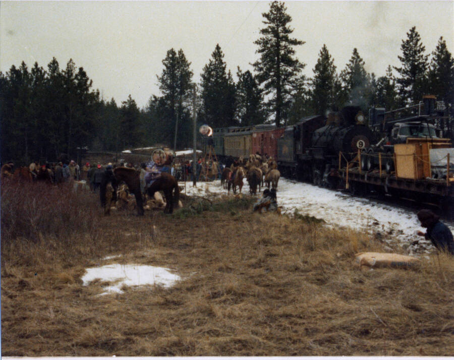 A photograph of a train stopped at the Craigmont Junction on the set of the film "Breakheart Pass". Description from Bill Clem: "Preparing for "Indian attacks" on train at Craigmont Junction prior to dynamiting of car carrying illegal rifles and ammunition in pine coffins. This car is immediately behind locomotive."