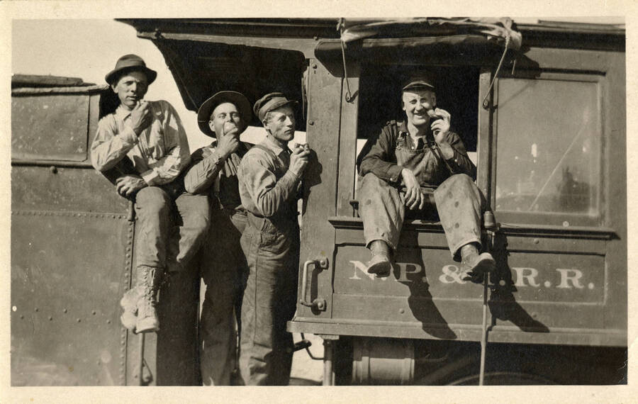 A postcard of several railroad workers eating a meal together on the train engine.