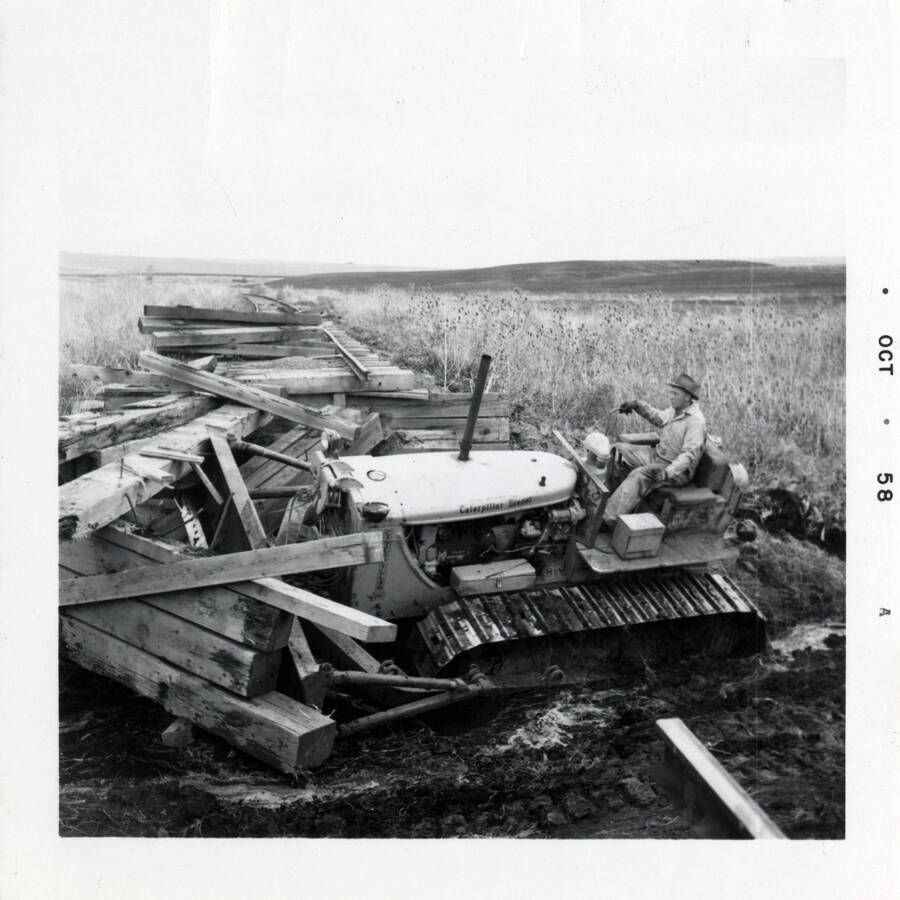 A photograph of a worker riding a tractor as he clears old railroad ties.