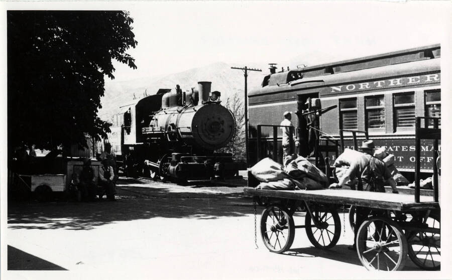 A photograph of 'train 311' unloading mail. 'Class L9, hand fired coal burning. Cab extended forward along boiler and engineer operated throttle by sitting in right cab window. Throttle up high along top of boiler. Uncomfortable for engineer and cold in winter.'