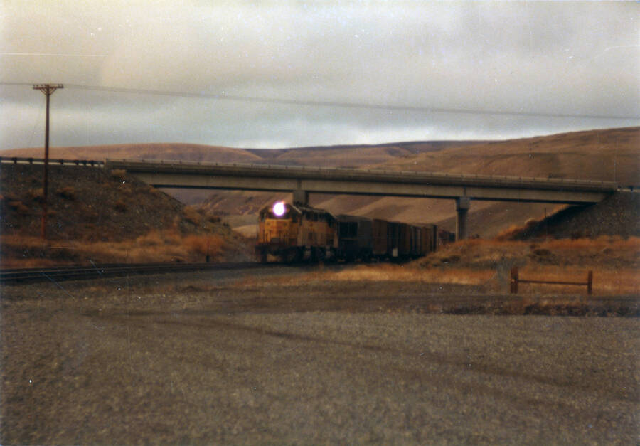 A photograph of Train #860 moving under the highway at Central Ferry, Washington. 55 miles west of Lewiston.