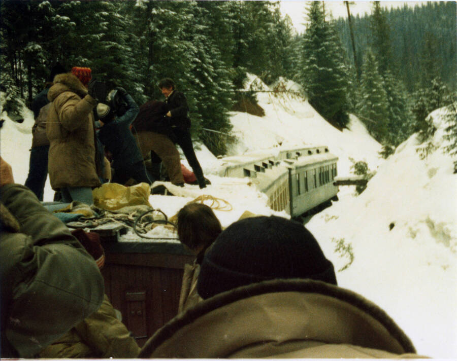 A photograph taken during the filming of the movie "Breakheart Pass."  A description from Bill Clem reads: "Taken from tender of Locomotive #9 as Charles Bronson "Deakin" fought with Archie Moore "Carlos" atop a snow covered boxcar (also equipped with emergency handrails along either side of top of car) as train was moving very carefully—about 10-12 miles per hour— on descending grade between Summitt and Headquarters, Idaho. "Carlos" lost the fight and was thrown over side of car while passing over Bridge 36."