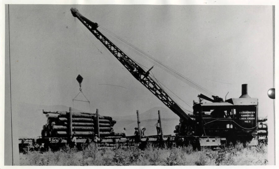 A photograph of a locomotive crane lifting wood at the unloading dock in Potlatch, Idaho.