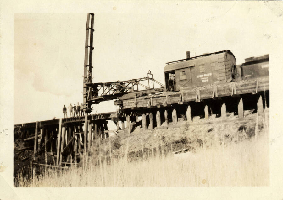 A photograph of pile driving occurring on bridge 66 of the Camas Prairie Railroad. Five unidentified workers stand atop the railroad scaffolding.