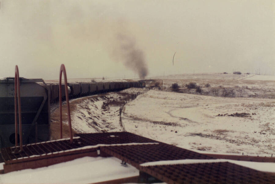 A color photograph of a freight train going around a bend in an open snowy landscape, taken from the caboose of the train.