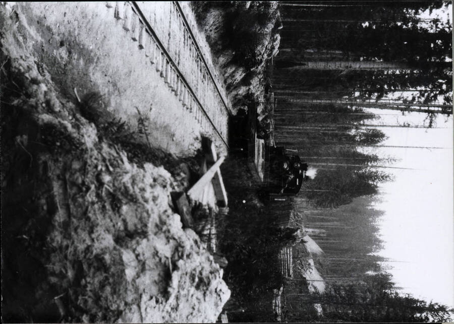 A photograph of a freight train approaching the camera in mountainous terrain. The snow covering much of the ground suggests the photo was taken during the winter months.