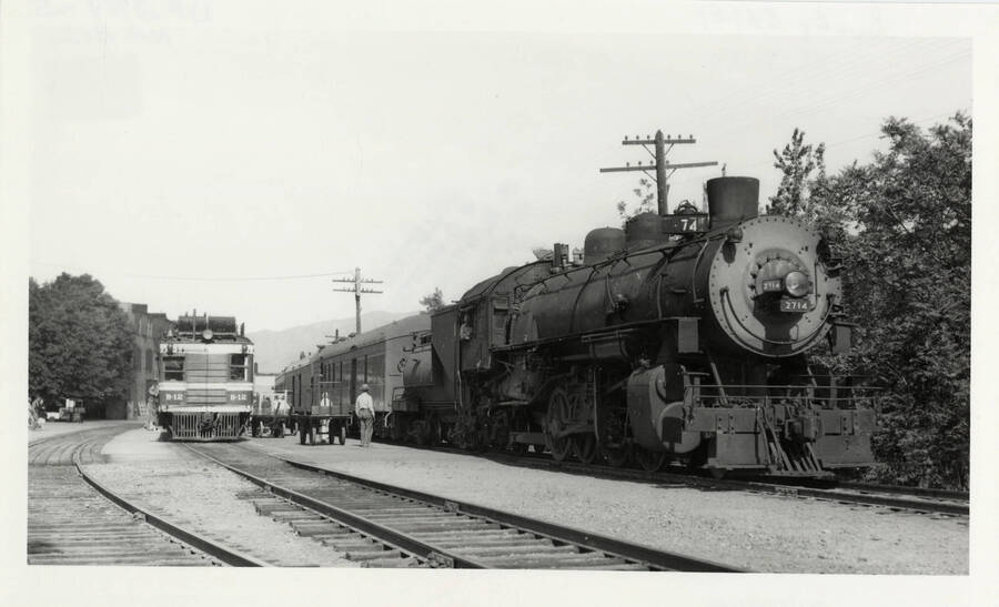 Passenger locomotive No. 2714 pictured with B-21 railway post office locomotive just outside of Lewiston, Idaho with people and carts.