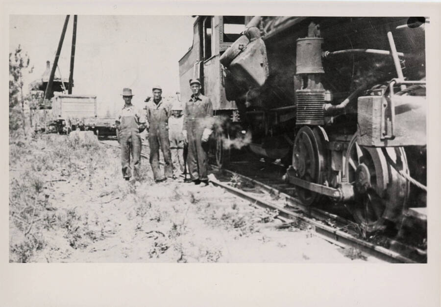 The Craig Mountain Railroad Heisler Engine #2 with four railroad workers standing to the left of the engine. One of these workers is Ansel McKenzie, the train engineer.