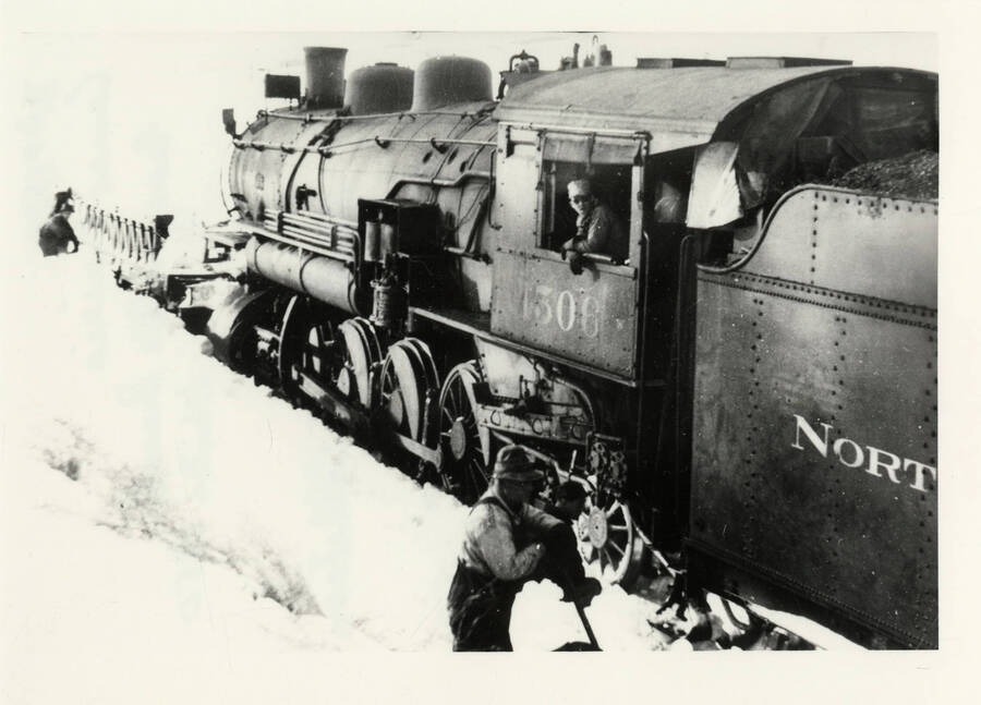 Northern Pacific Train Engine 1506 stuck in the snow on the Grangeville line in the winter of 1950. Several workers are pictured trying to dig it out of the snow.