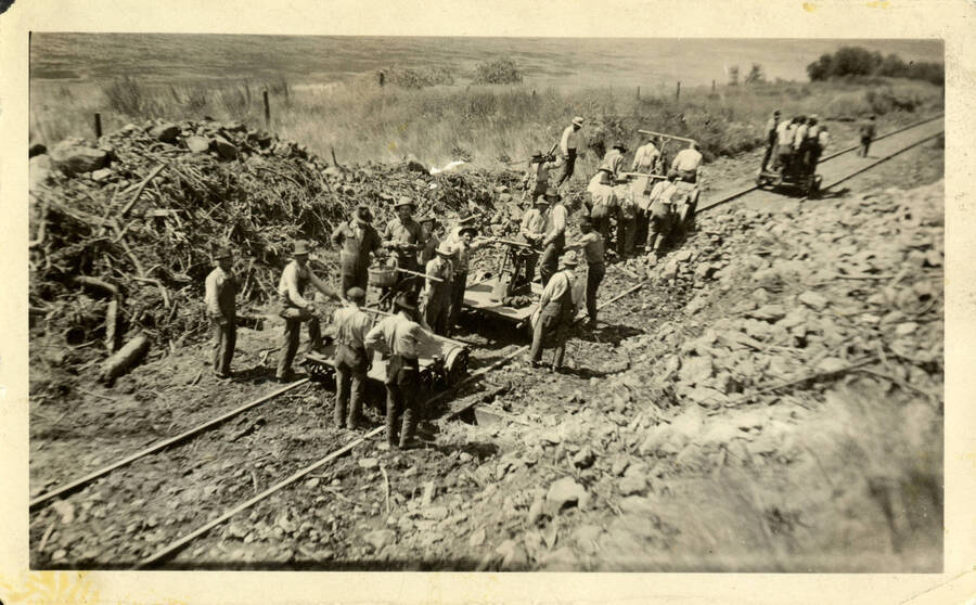 A photograph of several construction workers using handcars to begin the construction process of laying a railroad.