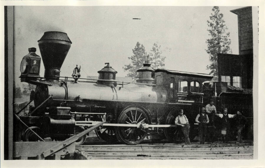 Northern Pacific engine #9 at the old Spokane Falls roundhouse on July 1, 1888. This engine pulled the first train into Genesee, Idaho on that date. The locomotive was shipped around the Horn and up the Columbia in 1879 to begin the building of the western end  of the railroad near Pasco, Washington. Rails were laid eventually to the coast and to connect with the west-bound crews at Gold Spike [sic] Montana. Note the old 'baloon' stack which was known as the 'Cushion Stack' at the time.'