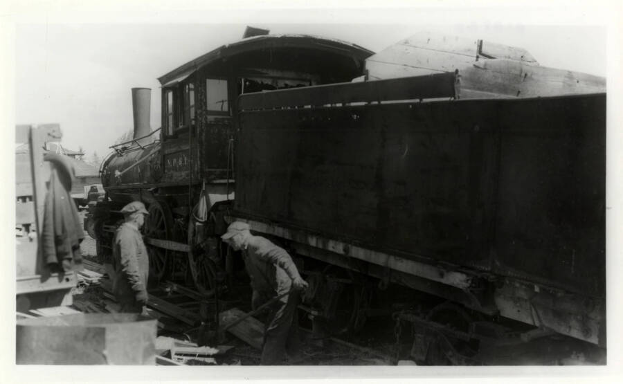 A photograph of Herb Banks and his team struggling to keep the train engine on the tracks when attempting to transport it to the 4-spot, to move it to Lewiston.The picture shows a derailed train engine, with the workers trying to place it back onto the tracks.