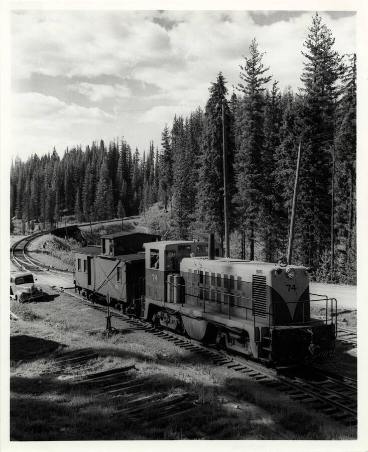 A photograph of a 'Whitcomb 70-ton Diesel #74 with caboose #611, just in from Camp 60 with a log tain. Engine #74 and two mates were delivered in 1948. They had 650 H.P. and were built with extra-heavy traction motors to lug up 5%-plus grades at 2-4 mph and were the first diesels to be used successfully in logging.'