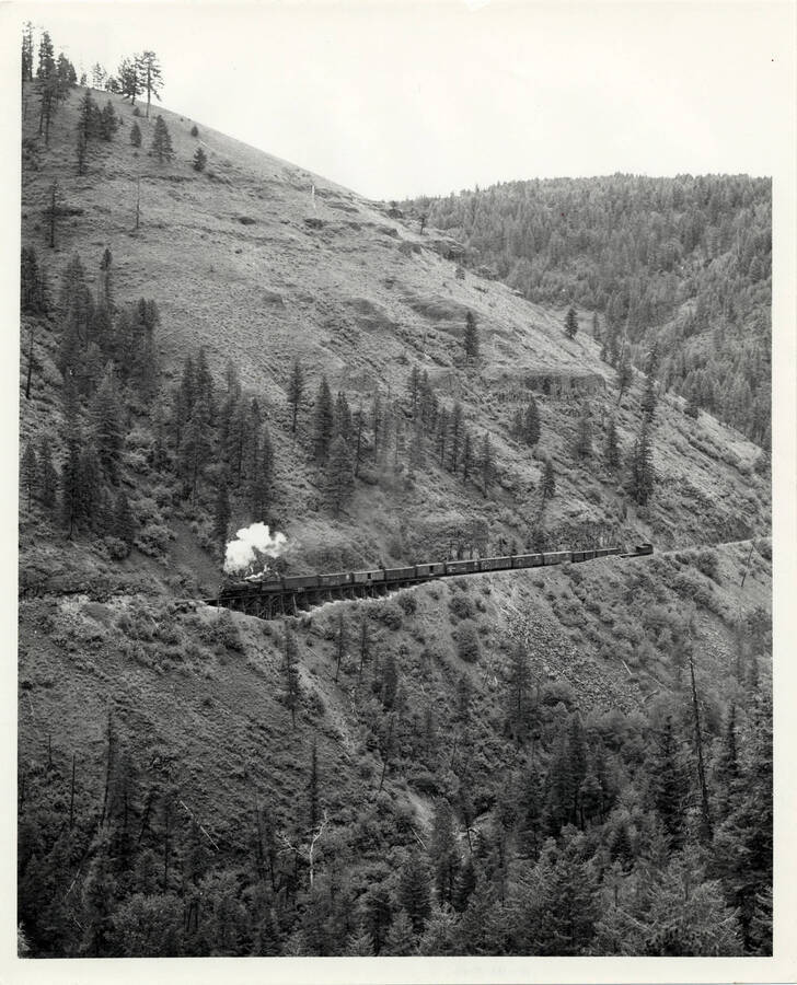 A photograph of train engine #1506 hauling 500 tons (its limit) of Grangeville local freight up the east wall of Lapwai Creek Canyon.