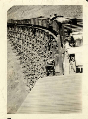 A photograph of a freight train exiting a bridge into tunnel 22 to Grangeville. This picture is taken with the train approaching the camera headon, with the line of cars seen stretching through the background.. The tunnel is not seen at all from this angle.