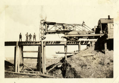 A photograph of pile driving occurring on bridge 66 of the Camas Prairie Railroad. Four unidentified men stand atop the railroad scaffolding.