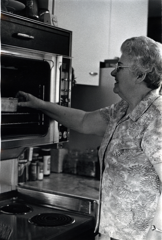 Photograph of Eunice Berry reaching for a pan in an oven.
