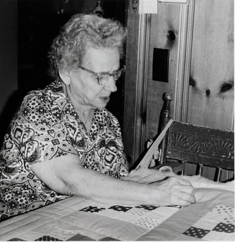 Photograph of Edna Cochrane looking down at a quilt.
