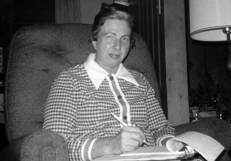 Photograph of May Hartman sitting, looking at the camera, holding a pencil and paper.