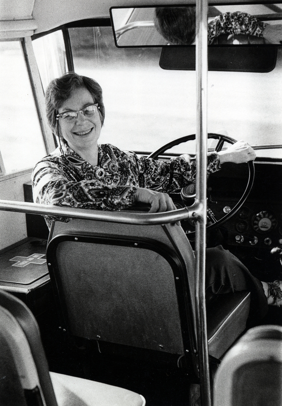 Photograph of Rita Mercedes Roach smiling at the camera, looking at the camera from the driver's seat in a bus.