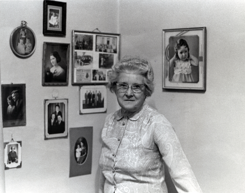 Photograph of Emilie Wright smiling at the camera, standing infront of framed photographs.