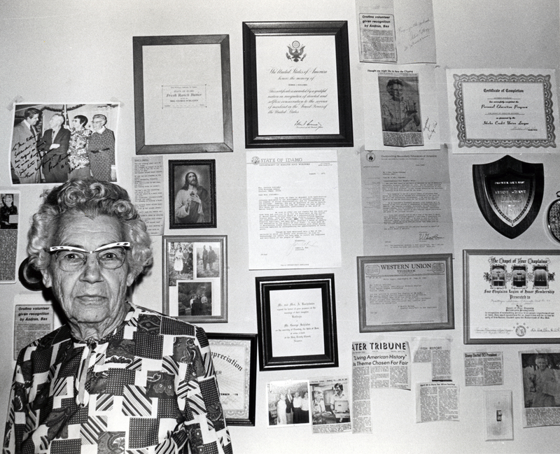 Photograph of Kathryn Schlader looking at the camera, in front of a wall of plaques.