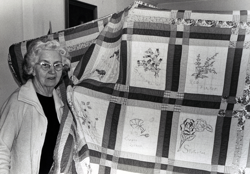 Photograph of Myrtle Cressler Warren standing in front of a quilt.