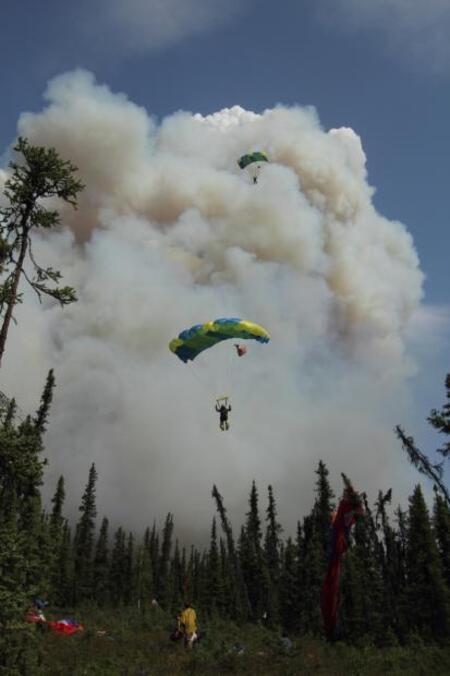 An example of smokejumpers approaching landing zone in clearing with smoke column in background. 5-31-2011. Photo: Mike McMillan