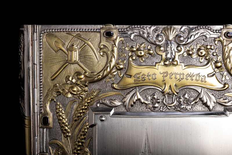 Close up detail of jewelry box cover corner featuring golden relief of a mining pick and shovel, along with a latern. 