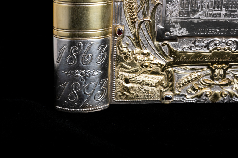 Close up detail of jewelry box cover corner featuring golden relief of logs and an ax. Cover is open and object is standing up as if it were a book, making the stylized spine also visible. Silver etching of the dates 1863 and 1893 pictured.