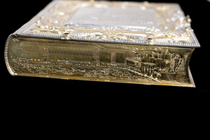 Close up detail of one short edge of object which appears as the bottom edge of the book. Featuring an etched scene of a train pulling both freight and passenger cars.