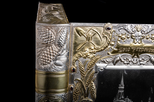 Close up detail of jewelry box cover corner featuring golden relief of mining pick, shovel, and latern. Cover is open and object is standing up as if it were a book, making the stylized spine also visible. Silver relief of pine cones pictured. 