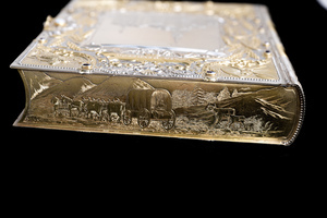 Close up detail of one short edge of object which appears as the top edge of the book. Featuring an etched scene of a covered wagon and emigrant family.