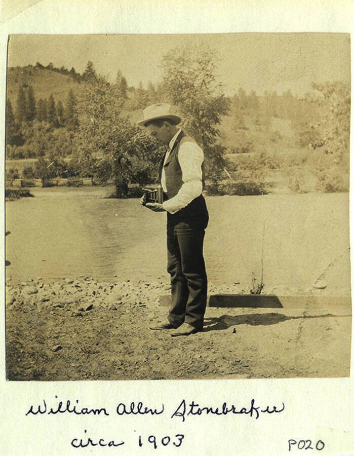 William Allen Stonebraker holds a camera on a river bank of the South Fork of the Clearwater River in Stites, Idaho. The photo caption reads: 'William Allen Stonebraker circa 1903.' 