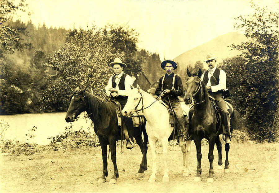 W. A. Stonebraker (left), Sumner Stonebraker, and J. M. Woodburn, M.D. pose on horseback near the riverbank.