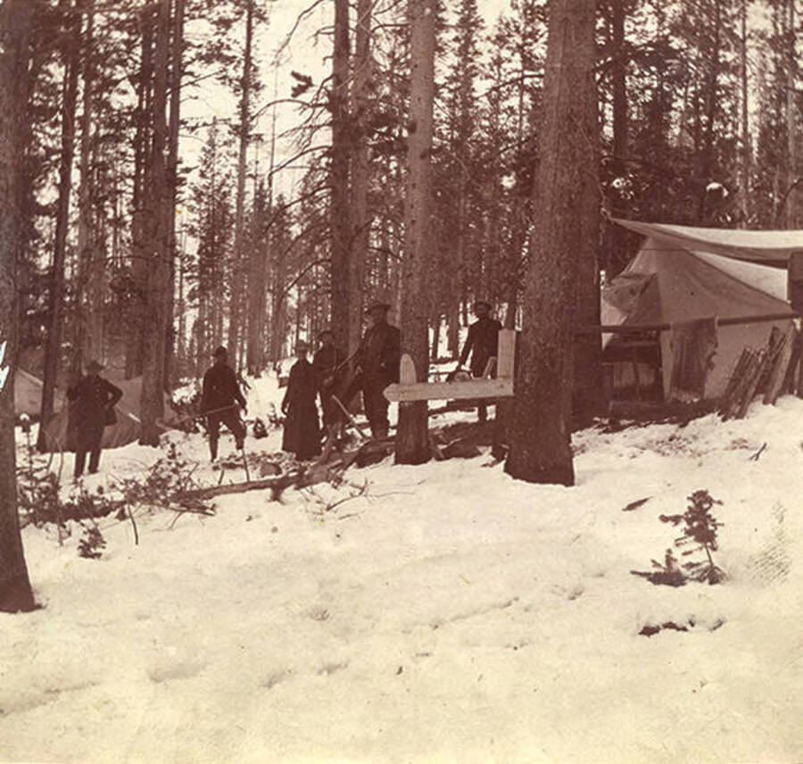 Five men and one woman pose near a tent camp in the snow on the Fourth of July. The woman may be Viola Lamb.
