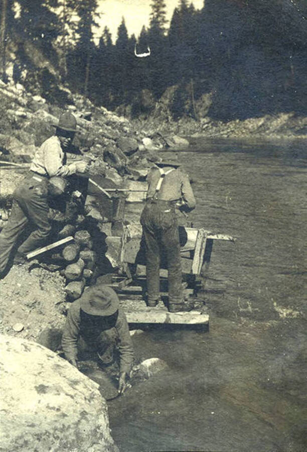 Three men with pan and sluice in the river.