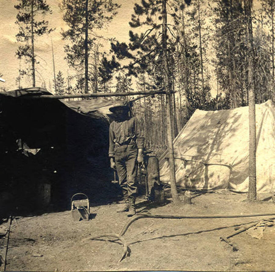A man stands outside a tent with blacksmith equipment in the foreground. Photo caption reads: 'Blacksmith shop.'