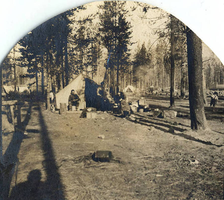 Men sit outside canvas tents in a forested area near Roosevelt, Idaho.