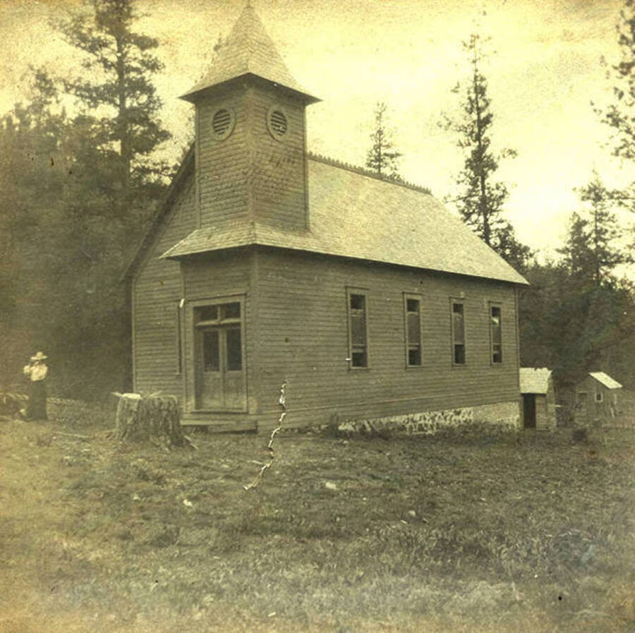 Lillian Stonebraker and Mr. Whitcomb stand to the left of the church. Two out buildings can be seen in the back. The photo caption reads: 'Indian Church.'