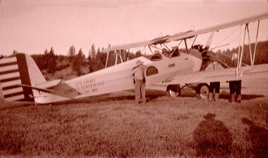 Adolph Stonebraker (Bill) stands near a National Guard 116th Observation Squadron. Plane reads 'U.S. Army Consolidated 0-17 NG 28-360' on its side. Plane is parked in the Chamberlain Basin meadow near the ranch house. The pilot was Nick Mamer.