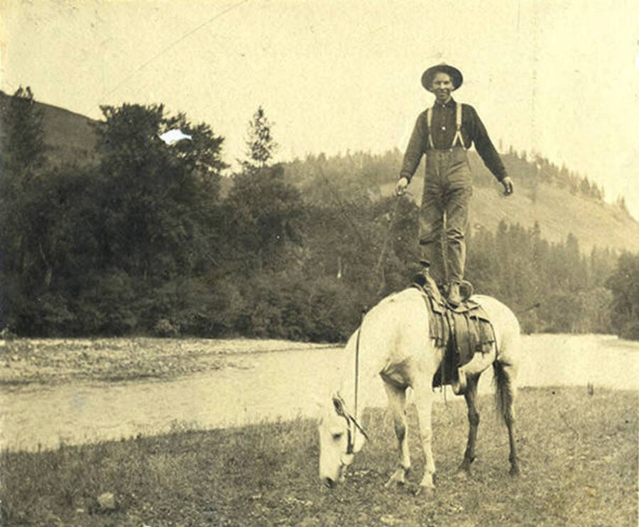 Sumner Stonebraker stands on the back of Whitey the horse alongside the Clearwater River.