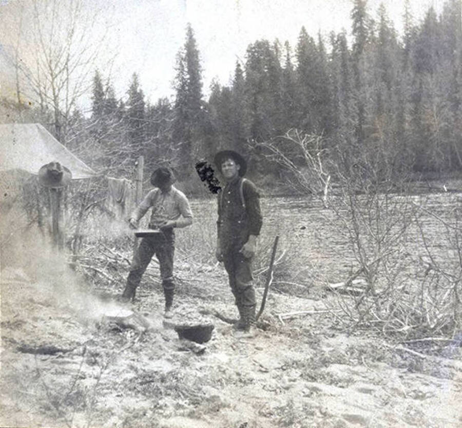 Two men cooking on river bank. The photo caption reads: 'The meat is burning.'