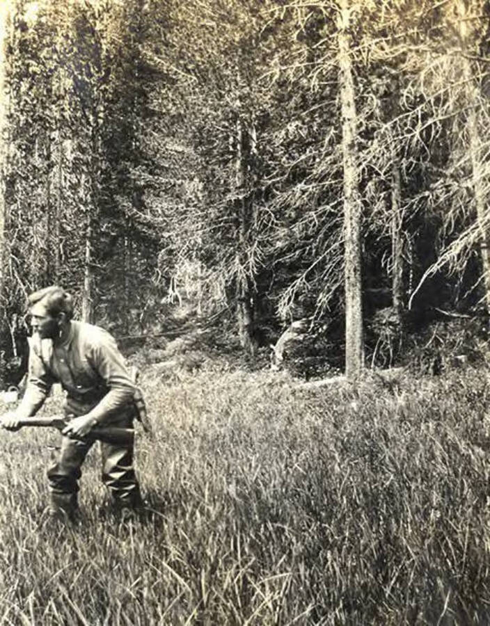 Man hunting with rifle in a grassy area near Fish Lake. The photo caption reads: 'Just keep still and I will get him.'