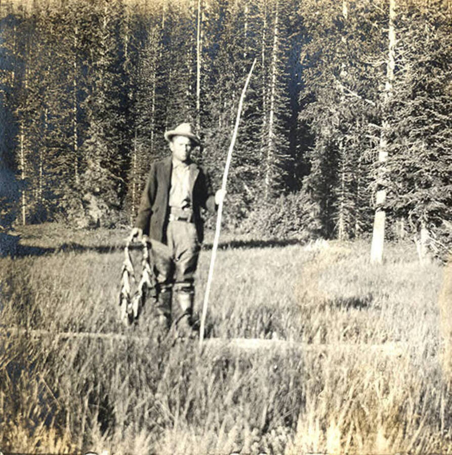 W. A. (Allen) Stonebraker stands with fishing rod and caught fish near Fish Lake.