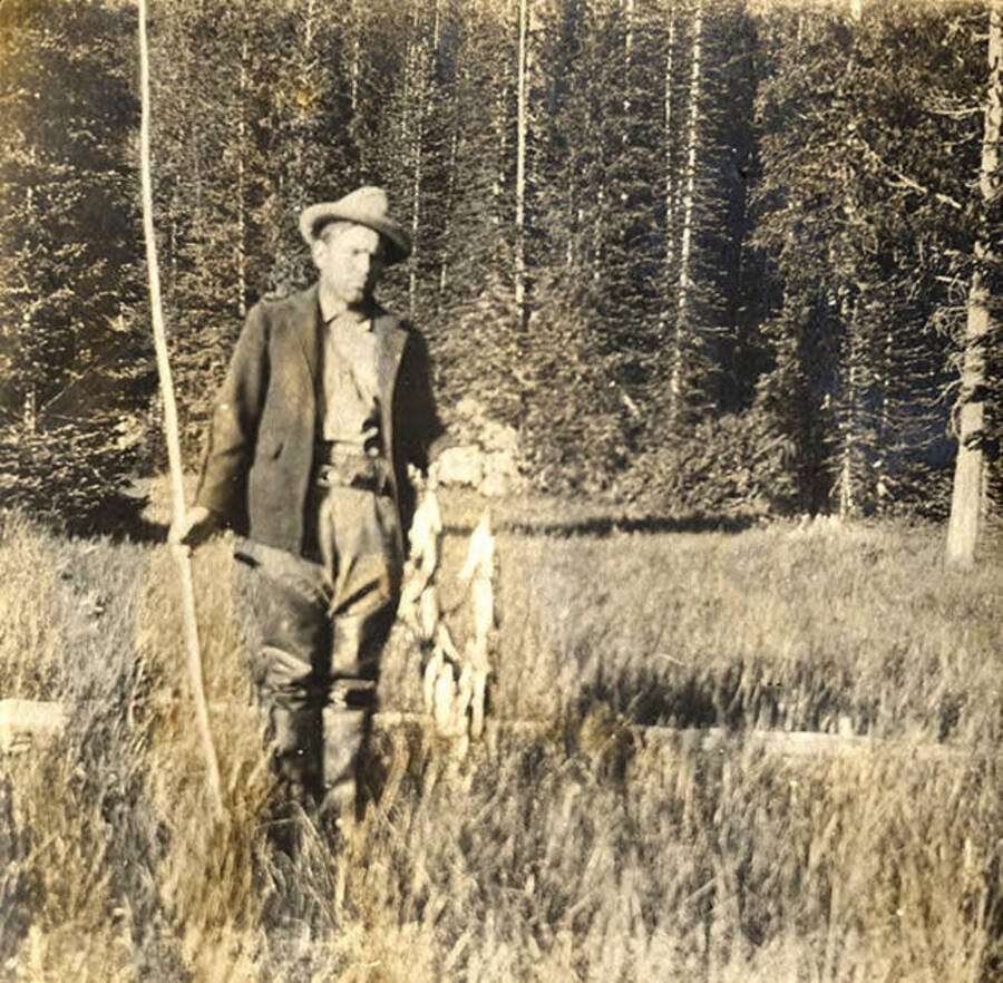 W. A. (Allen) Stonebraker stands with fishing rod and caught fish near Fish Lake.