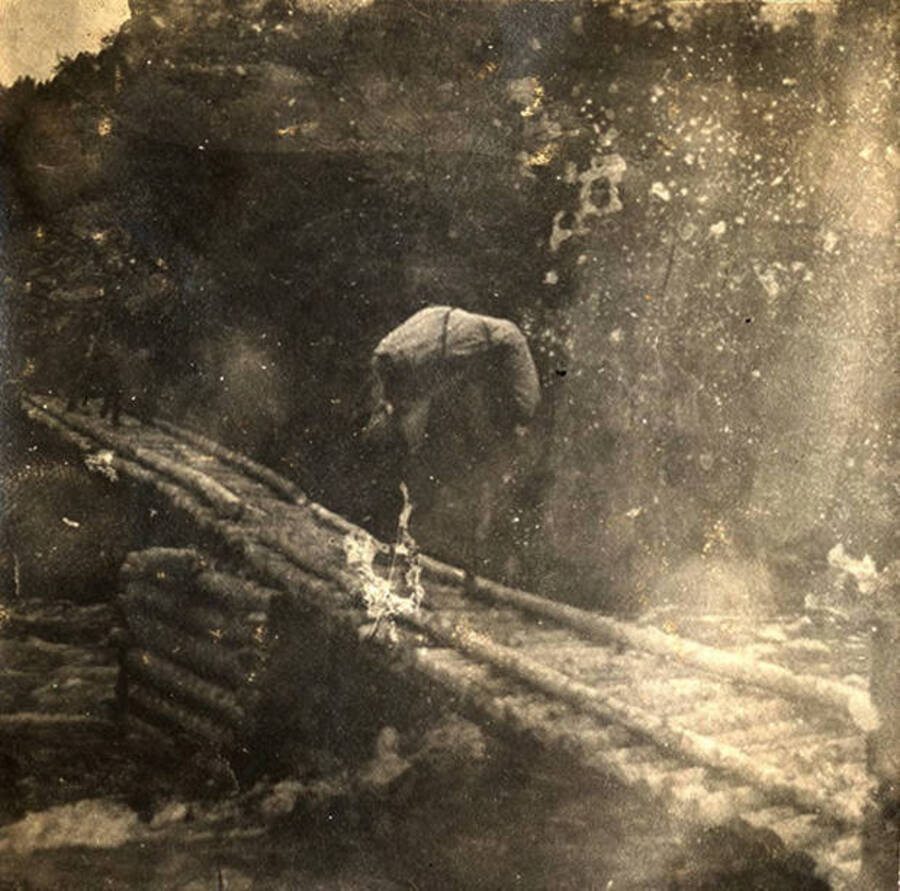 A horse carrying supplies crosses a wooden bridge over the river.
