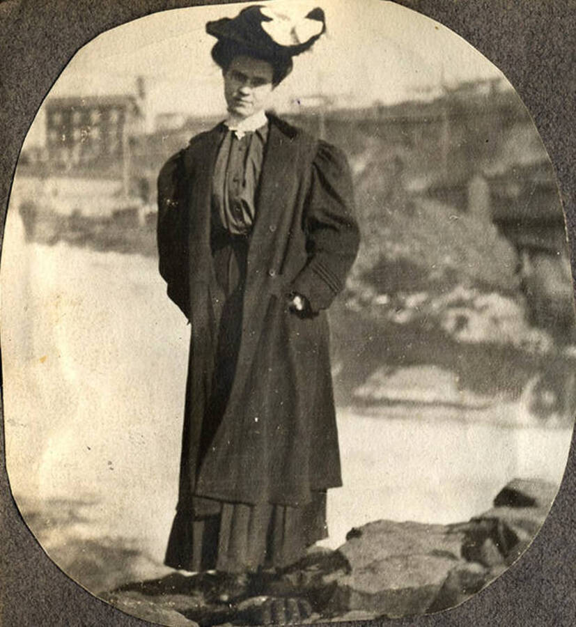 An unidentified woman stands on a rock below Spokane Falls.